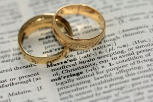 wedding rings on top of a page in a dictionary with the word 'marriage'. Online couple therapy can lead to a happy marriage