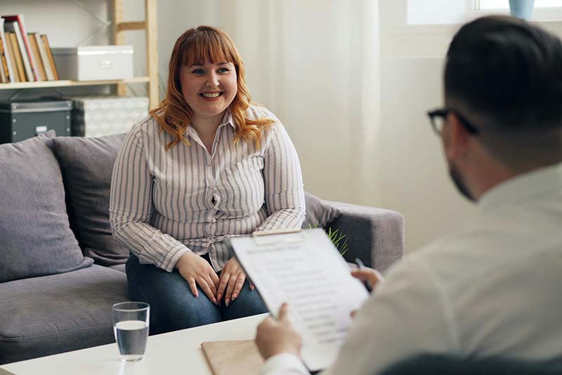 Happy lady sitting on couch having CBT Therapy in Manchester